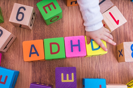 детски кубчета с букви, подредени така, че да образуват името ADHD, с ръката на детето